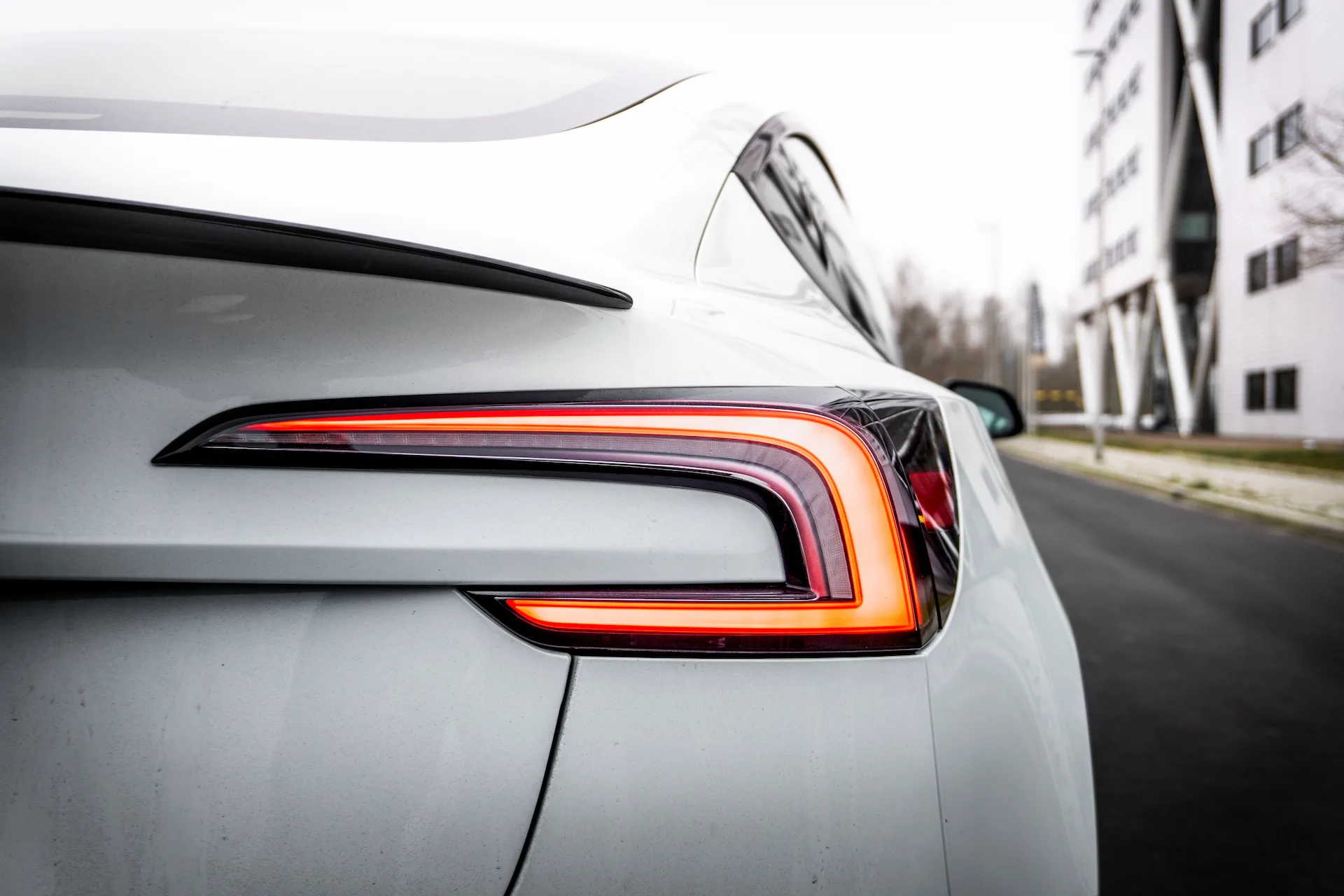 Leuchtende Rückleuchte und Heckspoiler eines weißen Tesla Model 3 in Nahaufnahme