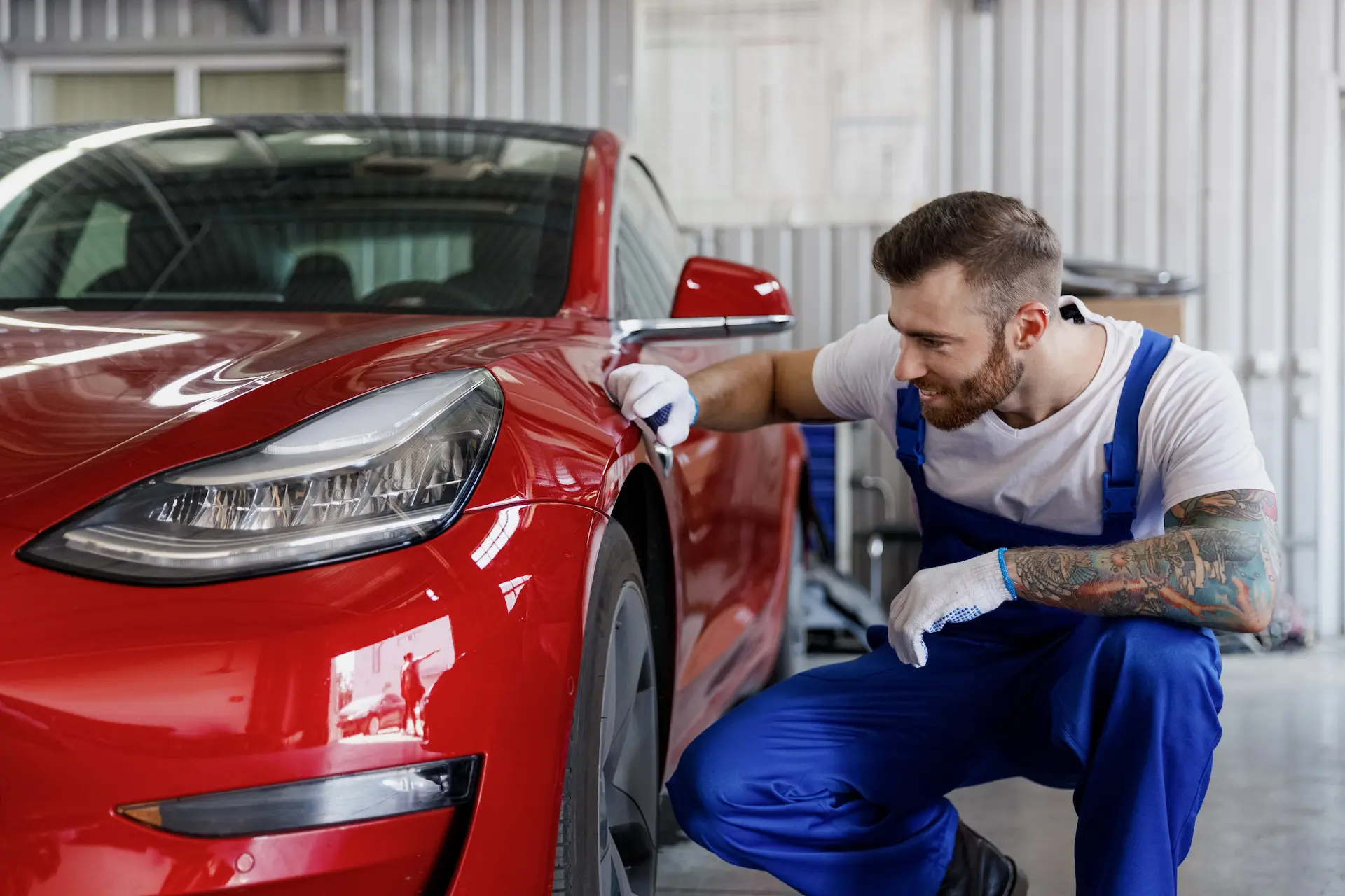 Mechaniker begutachtet die vordere Seitenpartie eines roten Tesla Model 3 in der Werkstatt