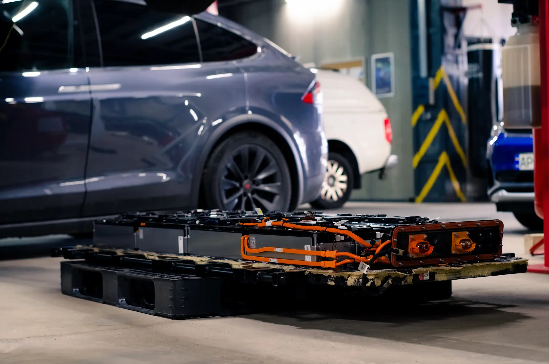 Ausgebautes Hochvolt-Batteriepaket eines Tesla, im Hintergrund ein Model X auf der Hebebühne