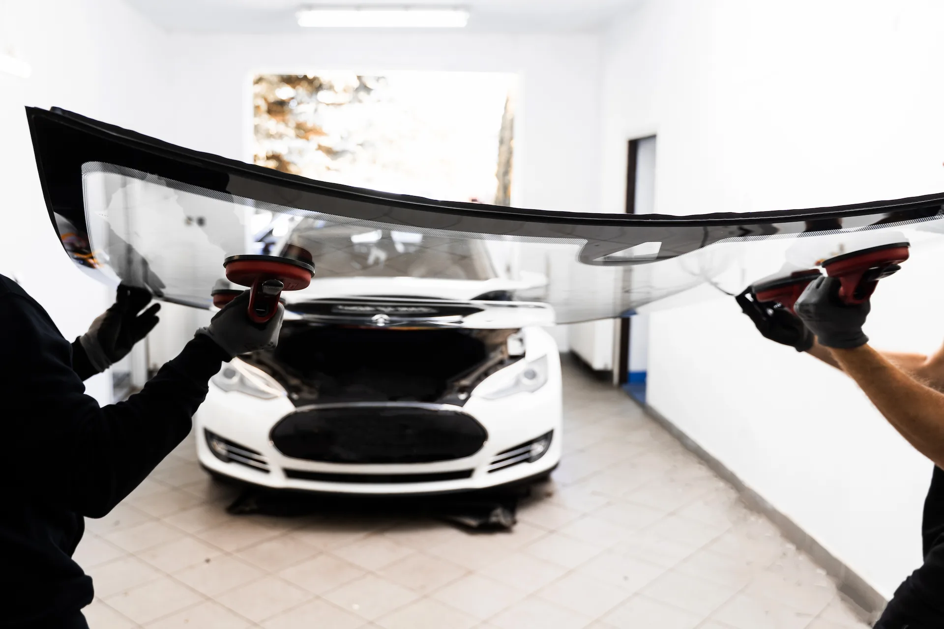 Zwei Techniker setzen mit Saughebern eine neue Windschutzscheibe in einen weißen Tesla Model S ein